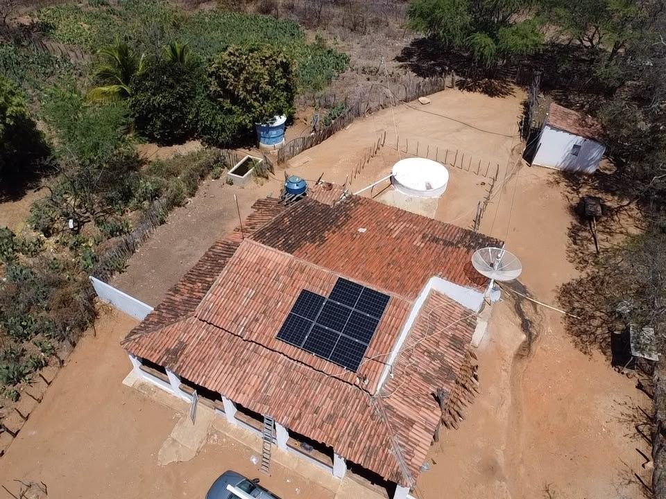 Vista de drone da casa do sítio em São Vicente Férrer, Itapetim, com oito módulos solares no telhado de telha e terreno de terra vermelha