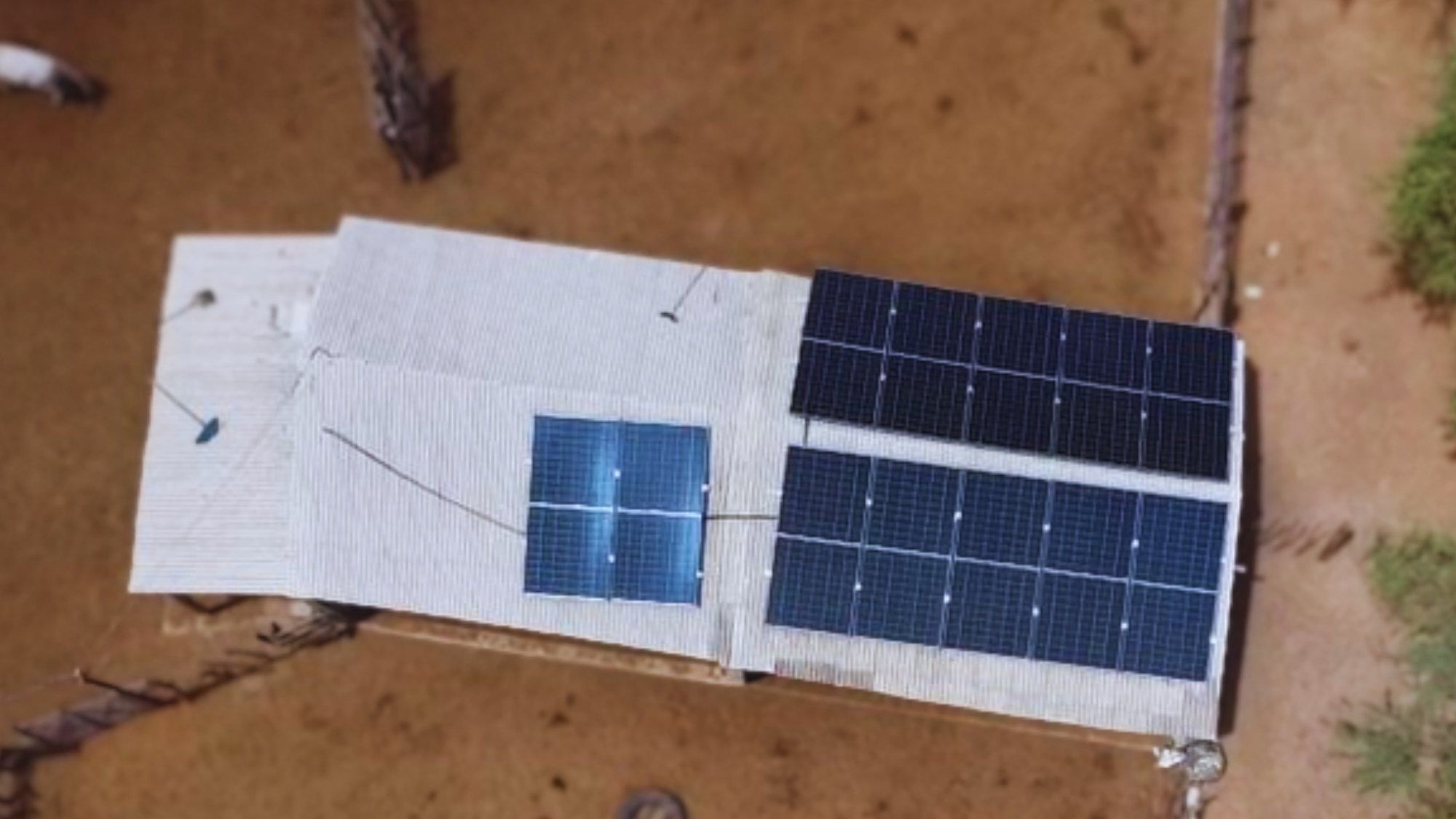 Vista de drone de casa no sítio em Tabira com módulos solares no telhado e chão de terra vermelha